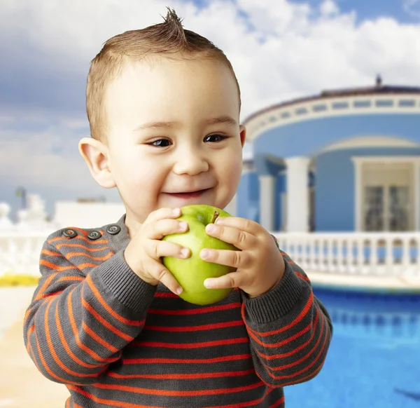 Портрет смешного ребенка с зеленым яблоком и улыбкой дома — стоковое фото