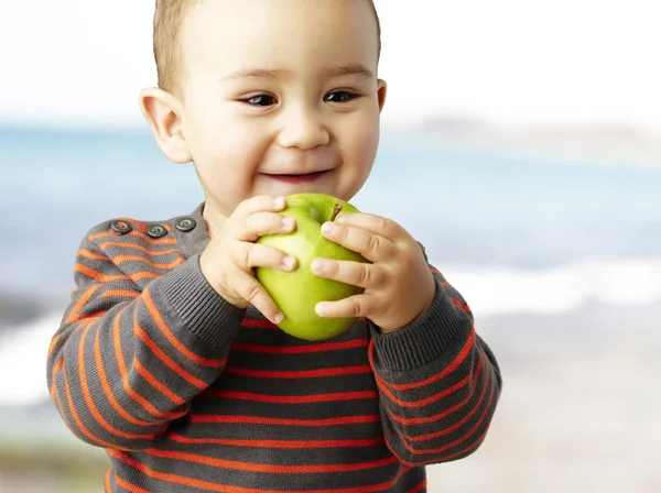 Portrait of funny kid holding green apple and smiling near the s — Stock Photo, Image