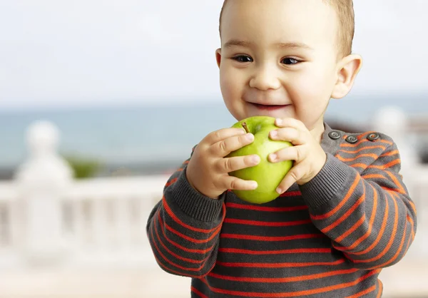 青リンゴを押しながら s に近い笑みを浮かべて面白い子供の肖像画 — ストック写真