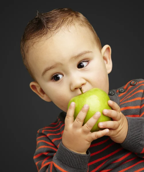 Portrait of a handsome kid bitting a green apple over black back — Stock Photo, Image