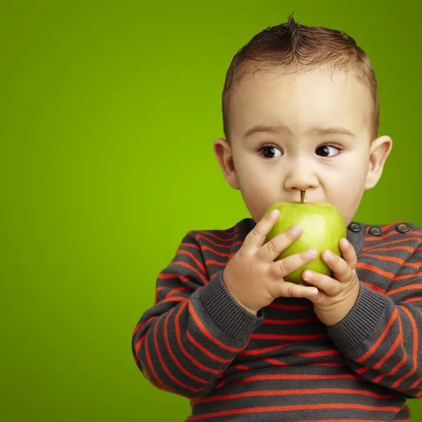 Retrato de um garoto bonito mordendo uma maçã verde sobre as costas verdes — Fotografia de Stock