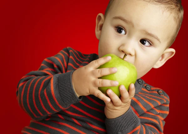 Porträtt av stilig liten bitting ett grönt äpple över röda bakgrunds — Stockfoto