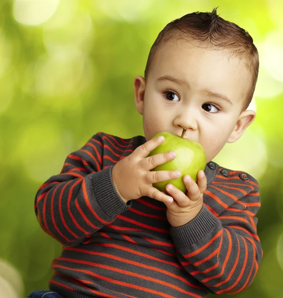 Portrait of a handsome kid bitting a green apple at park — Stock Photo, Image