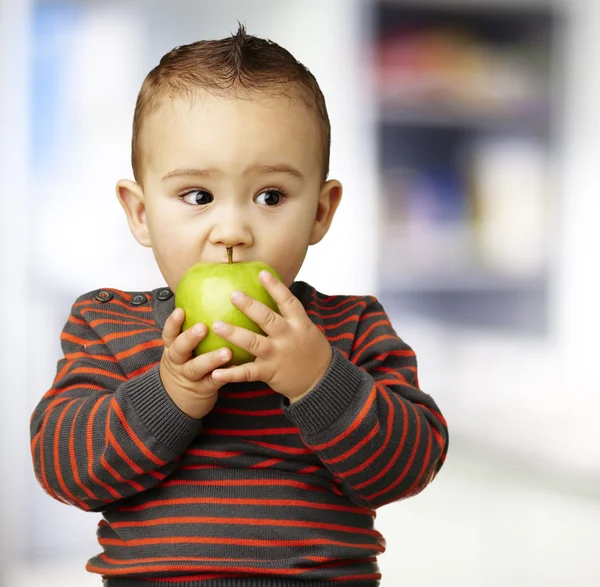 Portrait of a handsome kid bitting a green apple indoor — Stock Photo, Image