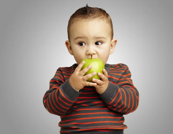 Портрет красивого ребенка, кусающего зеленое яблоко за серый рюкзак — стоковое фото