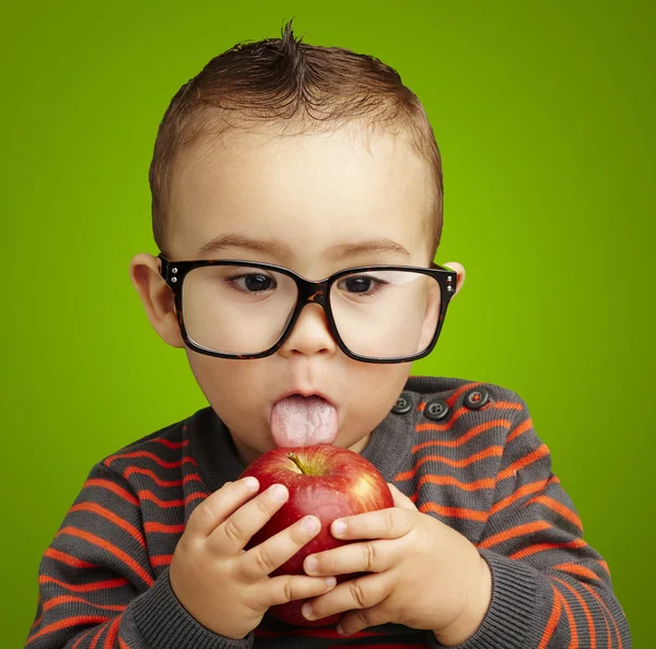 Portrait of a handsome kid wearing glasses sucking a red apple o — Stock Photo, Image