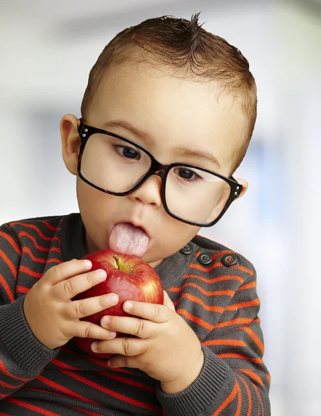 Portrait of a handsome kid wearing glasses sucking a red apple i — Stock Photo, Image