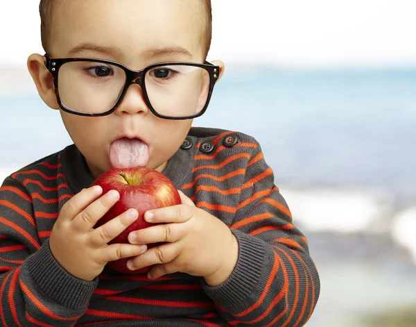 Портрет красивого ребенка в очках, сосущего красное яблоко — стоковое фото