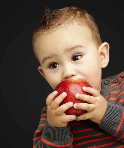 英俊的孩子，在黑色高建群吮吸一个红苹果的肖像 — 图库照片