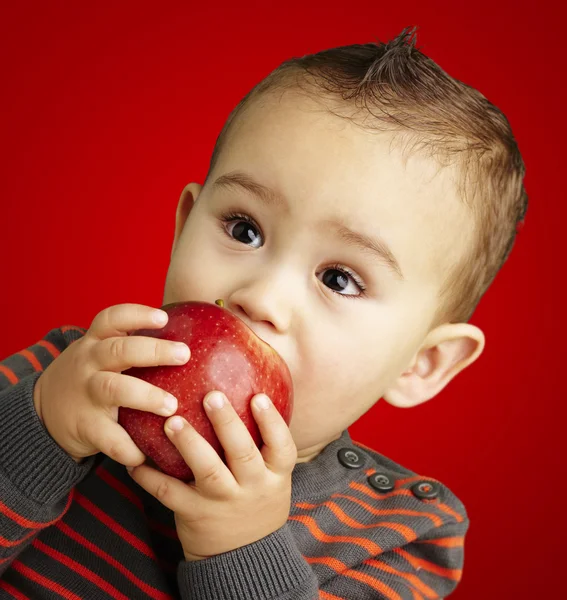 Portrait of a handsome kid sucking a red apple over red backgrou — Stock Photo, Image
