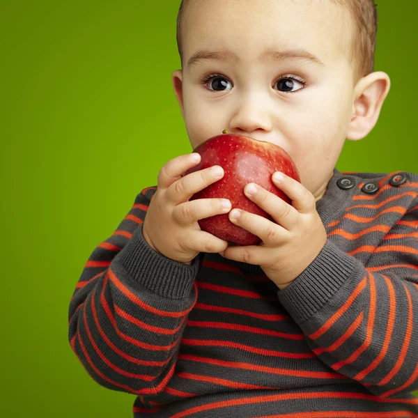Portrait of a handsome kid sucking a red apple over green backgr — Stock Photo, Image