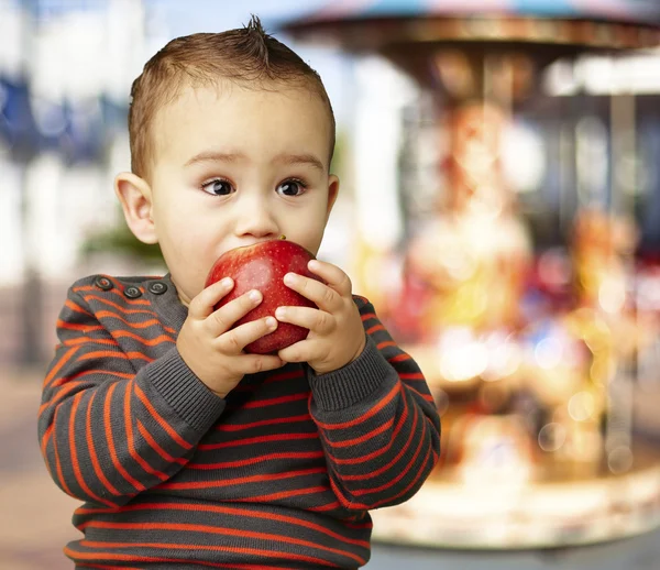 Porträtt av stilig liten suger ett rött äpple mot en carouse — Stockfoto