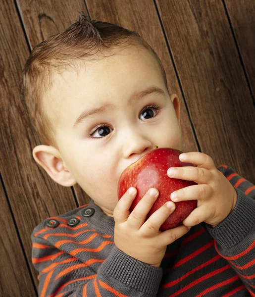 Portrait of a handsome kid sucking a red apple against a wooden — Stock Photo, Image