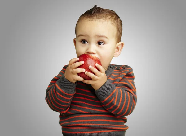 Portrait of a handsome kid sucking a red apple over grey backgro — Stock Photo, Image
