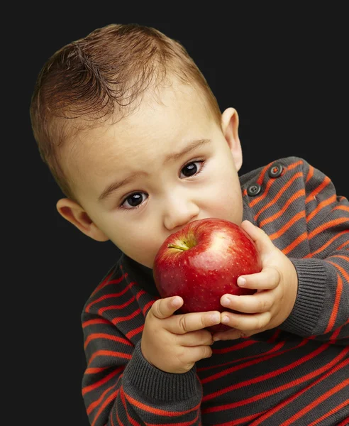 Portrait of a handsome kid sucking a red apple over black backgr — Stock Photo, Image