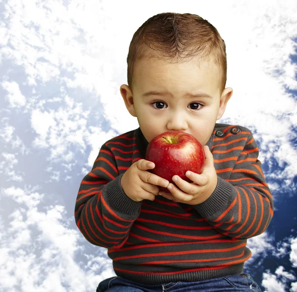 Portrait of a handsome kid sucking a red apple with a cloudy sky — Stock Photo, Image