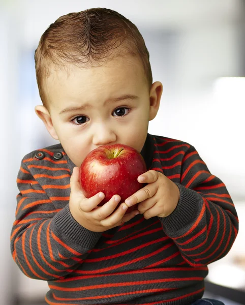 Portrait of a handsome kid sucking a red apple indoor — Stock Photo, Image