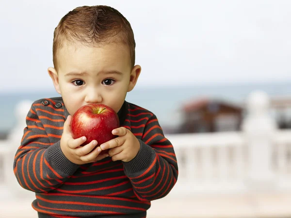 Retrato de um garoto bonito chupando uma maçã vermelha perto da praia — Fotografia de Stock