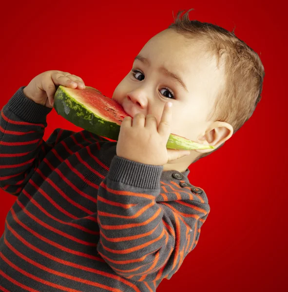 Portret przystojny dziecko bitting arbuza na czerwony backgro — Zdjęcie stockowe