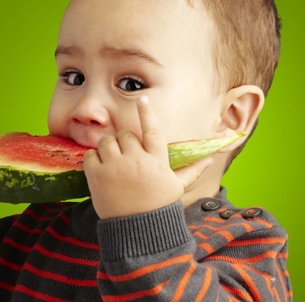 Портрет красивого ребенка, кусающего арбуз из-за зеленой спины — стоковое фото