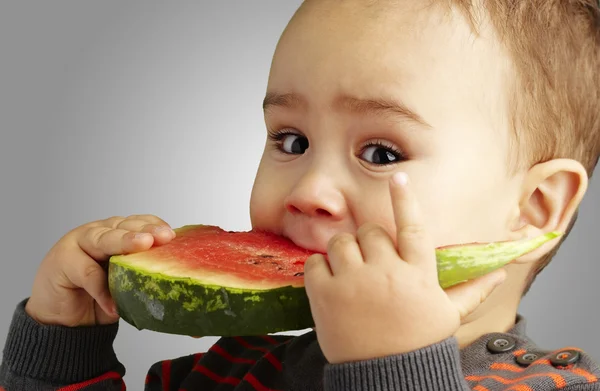 Porträt eines hübschen Kindes, das eine Wassermelone über einen grauen Backgr beißt — Stockfoto
