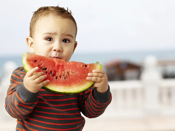 Porträtt av en stilig kid hålla en vattenmelon nära stranden — Stockfoto