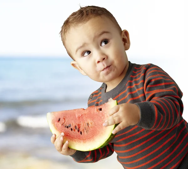 Portrait of a handsome kid holding a watermelon and tasting near — Stock Photo, Image