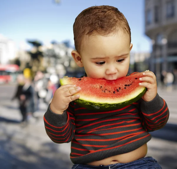 Porträt eines hübschen Kindes, das eine Wassermelone gegen eine Krähe beißt — Stockfoto