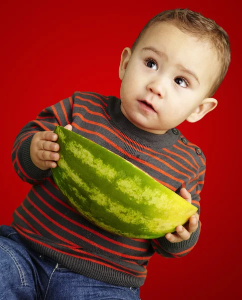 Portrait d'un nourrisson tenant une grosse pastèque sur fond rouge — Photo