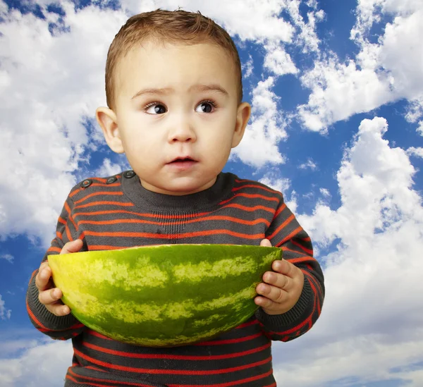 Retrato de un niño dulce sosteniendo una gran sandía contra una nublada —  Fotos de Stock