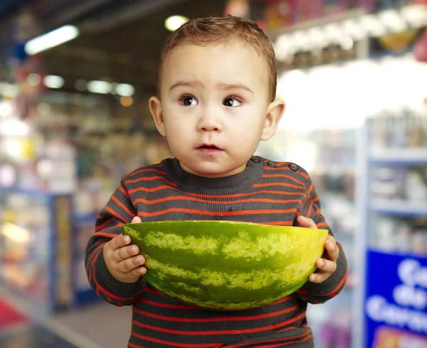 Porträtt av söt ungen håller en stor vattenmelon mot en butik — Stockfoto