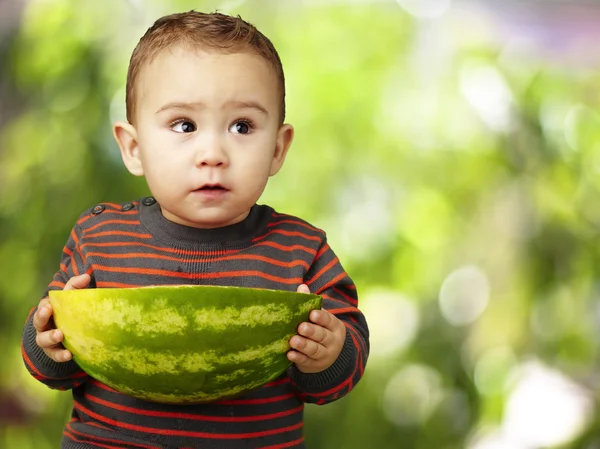 Retrato de un niño dulce sosteniendo una gran sandía contra una naturaleza — Foto de Stock