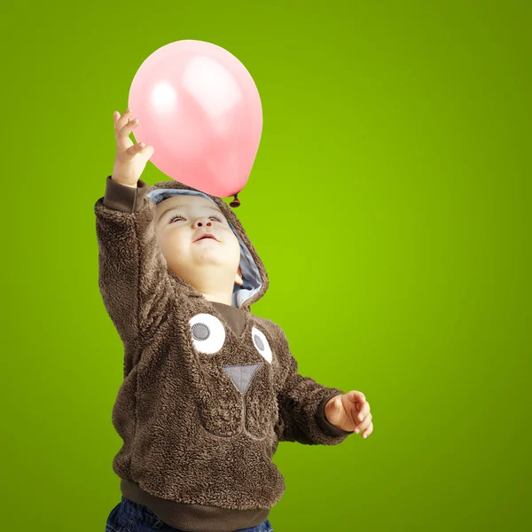 Porträt eines lustigen Kindes, das versucht, einen rosafarbenen Luftballon über ein grünes B zu halten — Stockfoto
