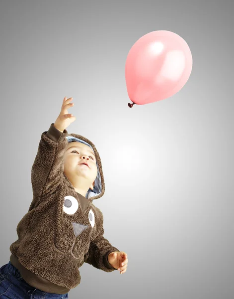 Retrato de un chico gracioso tratando de sostener un globo rosa sobre una ba gris —  Fotos de Stock