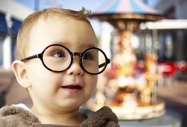 Portrait of kid wearing round glasses against a carousel — Stock Photo, Image