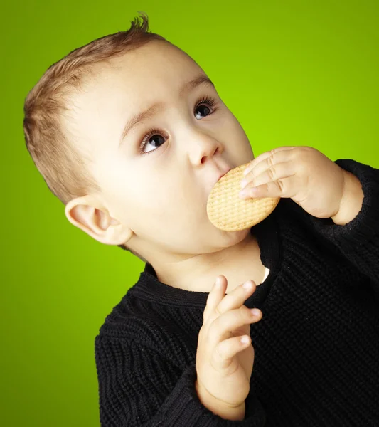 Porträt eines Kindes, das einen Keks vor grünem Hintergrund isst — Stockfoto