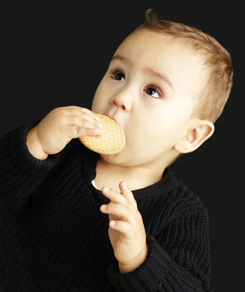 Portrait of kid eating a biscuit over black background — Stock Photo, Image