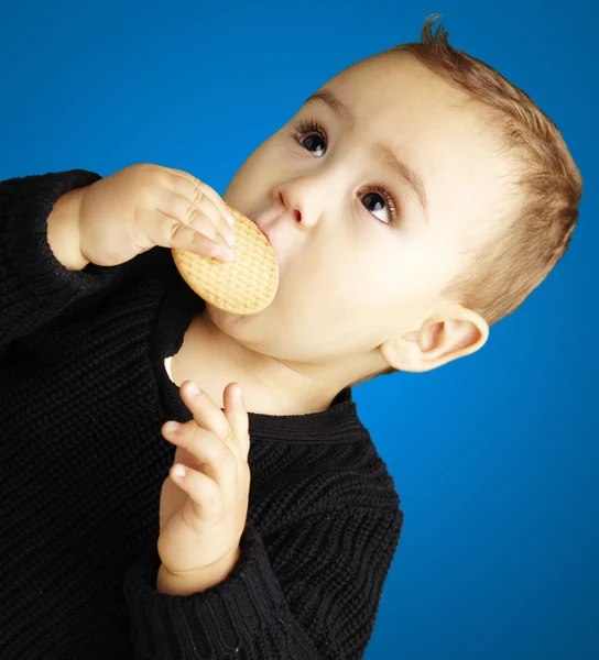 Retrato del niño comiendo una galleta sobre fondo azul — Foto de Stock