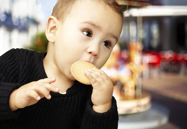 Retrato de criança bonita comendo um biscoito contra um carrossel — Fotografia de Stock