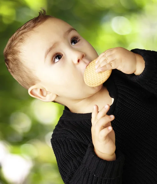 Porträt eines hübschen Kindes, das einen Keks vor einem Naturbackofen isst — Stockfoto