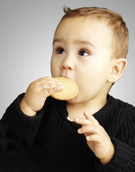 Retrato del niño comiendo una galleta sobre fondo gris — Foto de Stock