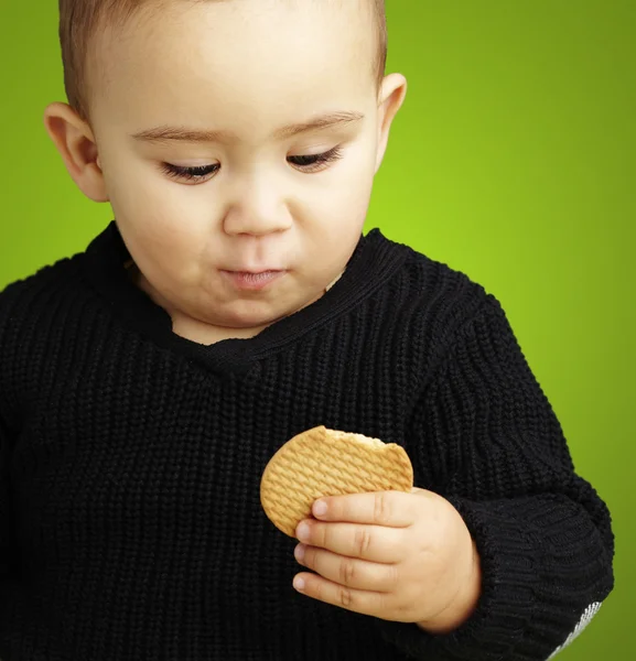 Porträt eines hübschen Kindes, das einen Keks vor einem grünen Backofen isst — Stockfoto