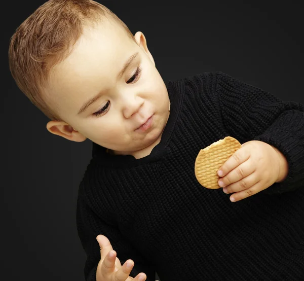 Retrato de garoto bonito comendo um biscoito contra um backgr preto — Fotografia de Stock