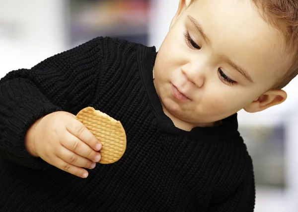 Πορτρέτο του όμορφος παιδί να φάει ένα μπισκότο ενάντια σε μια εσωτερική — Φωτογραφία Αρχείου