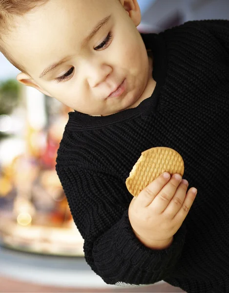 Portret van knappe jongen eten een koekje tegen een carrousel — Stockfoto