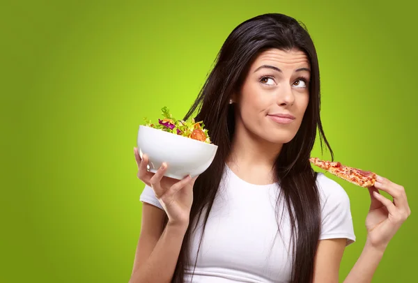 Retrato de mulher jovem escolhendo pizza ou salada contra um verde — Fotografia de Stock