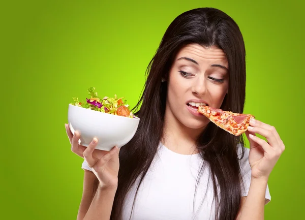 Retrato de una mujer joven comiendo pizza y buscando ensalada sobre gree — Foto de Stock