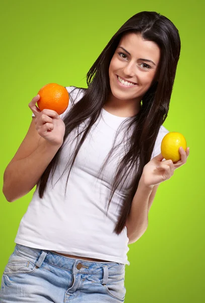 Young pretty girl holding orange and lemon over green background — Stock Photo, Image