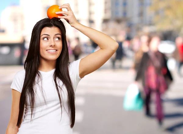 Retrato de mujer joven sosteniendo naranja en su cabeza en la ciudad —  Fotos de Stock