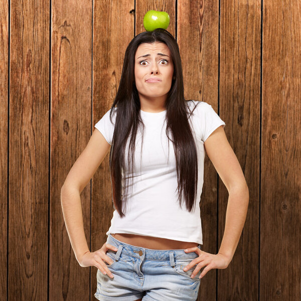 Portrait of young woman holding green apple on her head against